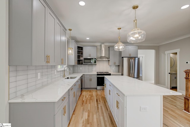 kitchen with stainless steel appliances, wall chimney range hood, decorative light fixtures, light hardwood / wood-style flooring, and a kitchen island