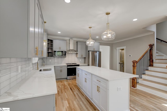 kitchen with stainless steel appliances, sink, wall chimney range hood, light hardwood / wood-style flooring, and a kitchen island