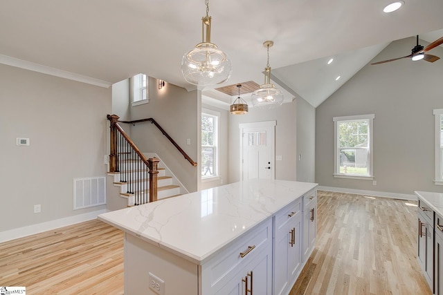 kitchen with pendant lighting, a center island, white cabinets, light hardwood / wood-style floors, and light stone counters