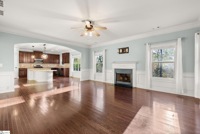 unfurnished living room featuring crown molding, ceiling fan, a healthy amount of sunlight, and dark hardwood / wood-style floors