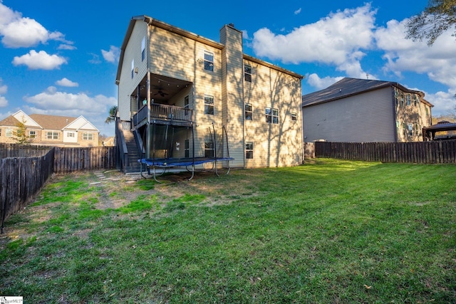 back of house with a yard, ceiling fan, a balcony, and a trampoline