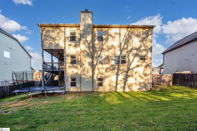 back of property with a trampoline and a yard