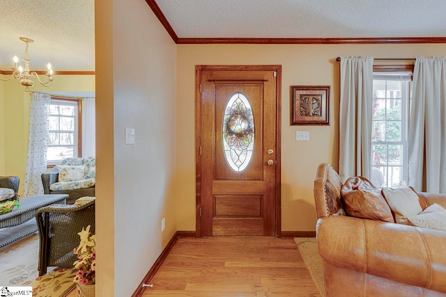 foyer entrance featuring light hardwood / wood-style floors, ornamental molding, a textured ceiling, and a chandelier