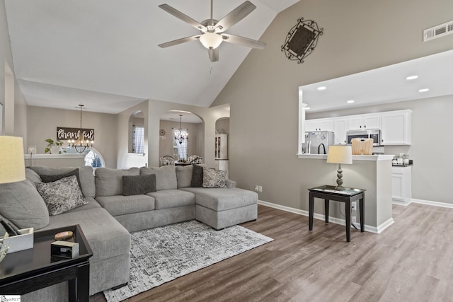 living room with high vaulted ceiling, ceiling fan with notable chandelier, and light wood-type flooring