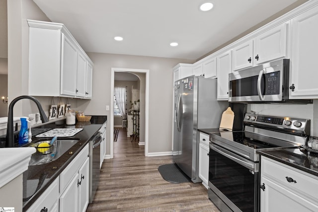 kitchen featuring dark stone counters, stainless steel appliances, sink, hardwood / wood-style flooring, and white cabinets