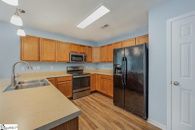 kitchen with decorative light fixtures, light wood-type flooring, stainless steel appliances, and sink