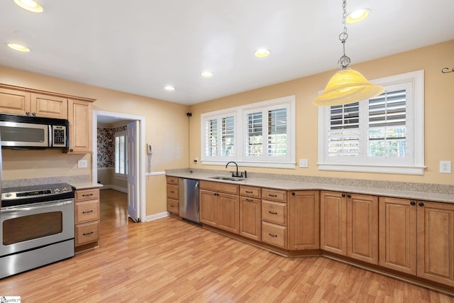 kitchen featuring sink, stainless steel appliances, decorative light fixtures, and light wood-type flooring