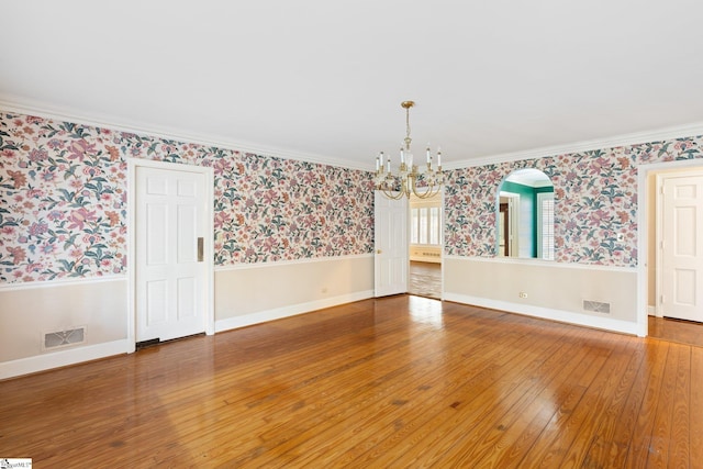 spare room with hardwood / wood-style floors, ornamental molding, and a notable chandelier