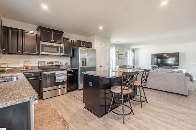 kitchen featuring light hardwood / wood-style flooring, light stone counters, appliances with stainless steel finishes, a kitchen island, and a kitchen bar