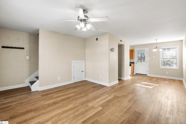 unfurnished living room with ceiling fan with notable chandelier and light hardwood / wood-style floors