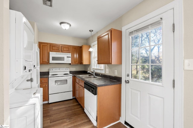 kitchen with white appliances, dark wood-type flooring, sink, stacked washing maching and dryer, and decorative light fixtures