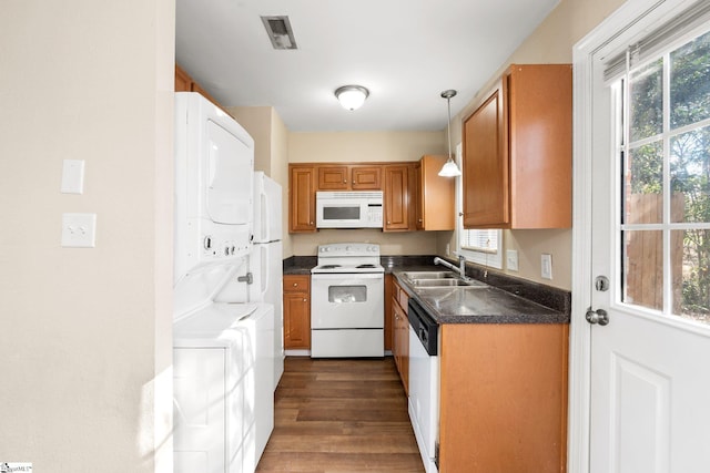 kitchen with sink, dark hardwood / wood-style flooring, stacked washer and dryer, decorative light fixtures, and white appliances