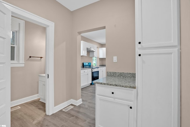 kitchen featuring stainless steel electric range, light stone counters, white cabinetry, and light hardwood / wood-style flooring