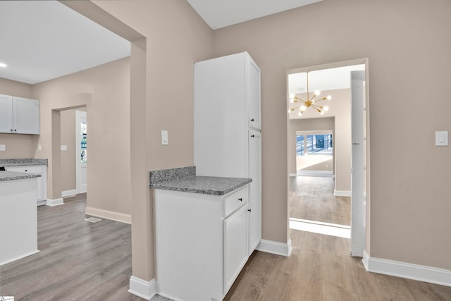 kitchen with light wood-type flooring, light stone counters, decorative light fixtures, an inviting chandelier, and white cabinetry