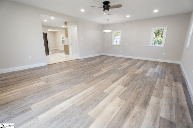 spare room featuring a wealth of natural light, light hardwood / wood-style floors, and ceiling fan with notable chandelier