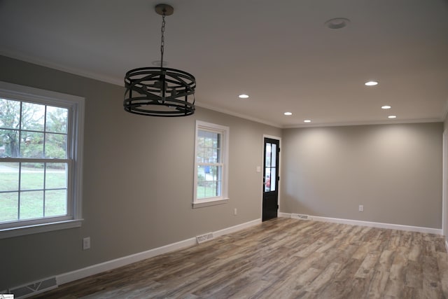 spare room featuring hardwood / wood-style floors, an inviting chandelier, a healthy amount of sunlight, and ornamental molding