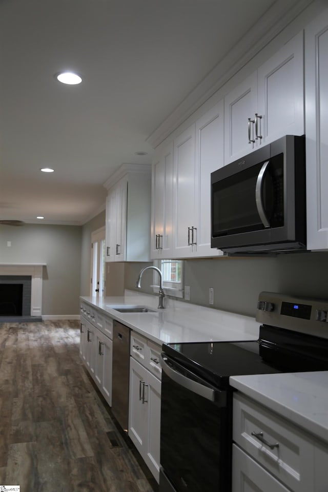 kitchen with dark wood-type flooring, white cabinets, sink, a brick fireplace, and stainless steel appliances