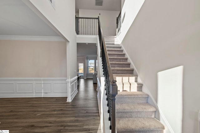 stairway featuring a high ceiling, hardwood / wood-style flooring, and ornamental molding