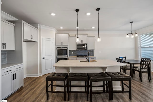 kitchen with dark hardwood / wood-style floors, an island with sink, decorative light fixtures, appliances with stainless steel finishes, and ornamental molding