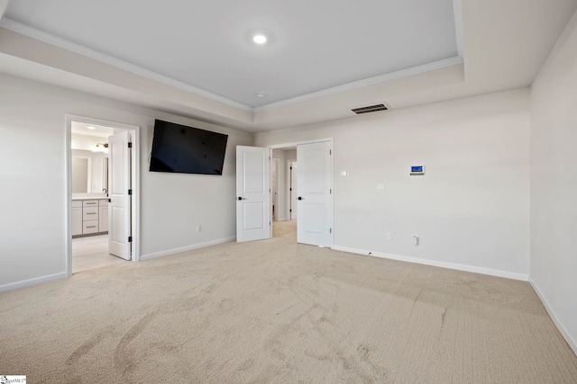 unfurnished bedroom featuring a raised ceiling, ensuite bathroom, crown molding, and light carpet