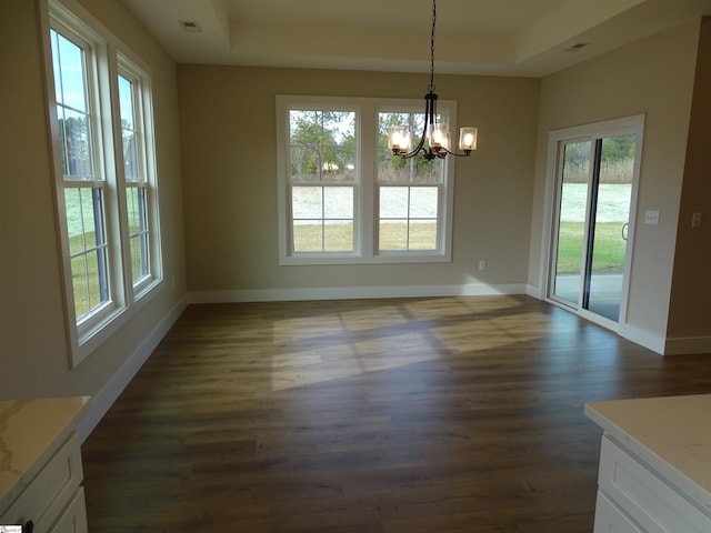 unfurnished dining area with a raised ceiling, an inviting chandelier, plenty of natural light, and dark wood-type flooring