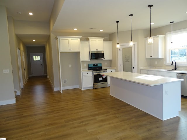 kitchen with appliances with stainless steel finishes, dark wood-type flooring, sink, white cabinets, and a center island