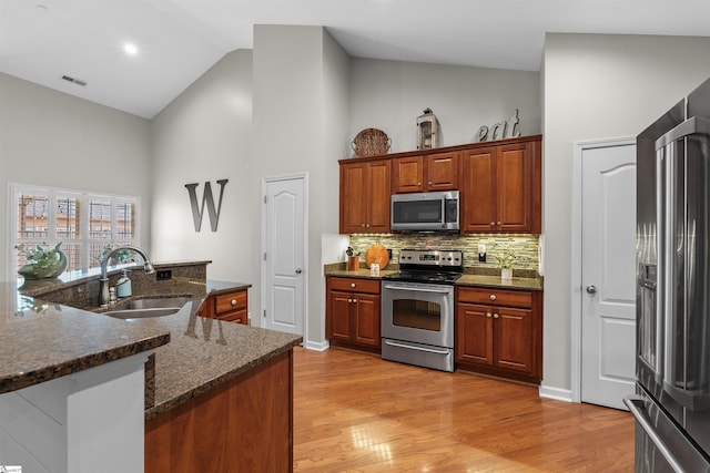 kitchen featuring appliances with stainless steel finishes, dark stone counters, sink, high vaulted ceiling, and light hardwood / wood-style flooring