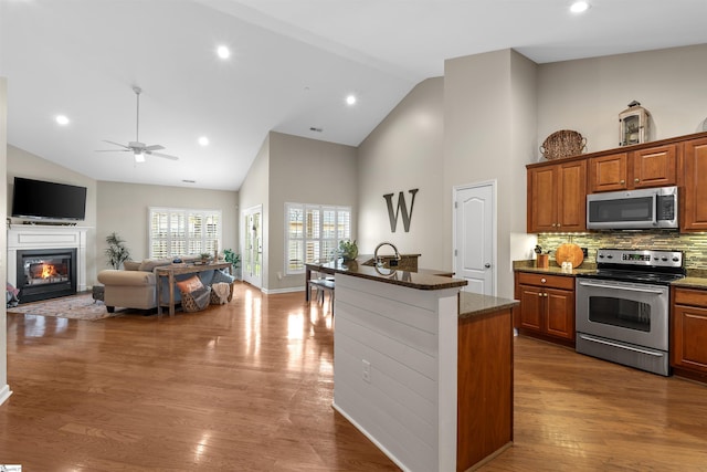 kitchen featuring backsplash, a kitchen island with sink, high vaulted ceiling, dark hardwood / wood-style flooring, and stainless steel appliances