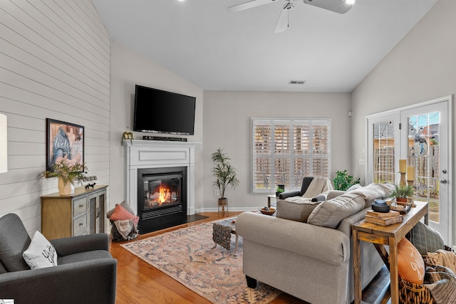 living room featuring hardwood / wood-style flooring, ceiling fan, wooden walls, and high vaulted ceiling