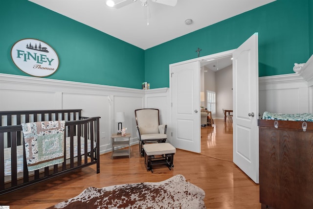 bedroom with ceiling fan, hardwood / wood-style floors, and a crib