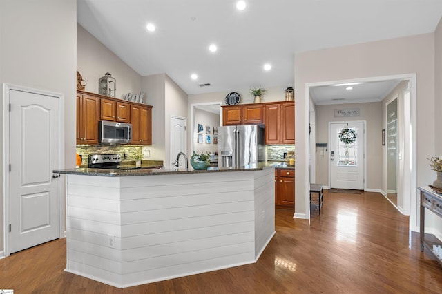 kitchen with hardwood / wood-style floors, decorative backsplash, stainless steel appliances, and an island with sink