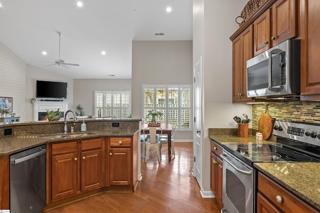 kitchen featuring stainless steel appliances, light hardwood / wood-style flooring, dark stone counters, and sink