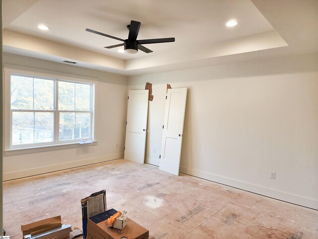 empty room with ceiling fan and a tray ceiling