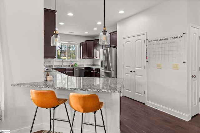 kitchen with kitchen peninsula, light stone countertops, stainless steel appliances, dark wood-type flooring, and hanging light fixtures