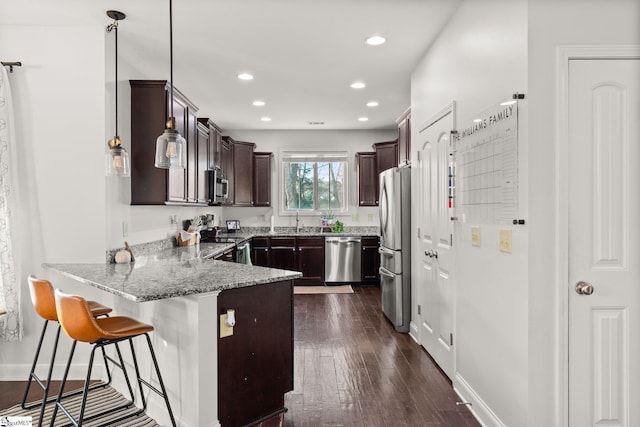 kitchen with light stone counters, dark hardwood / wood-style floors, pendant lighting, a breakfast bar area, and appliances with stainless steel finishes