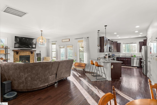 living room with french doors, dark wood-type flooring, sink, a notable chandelier, and a fireplace