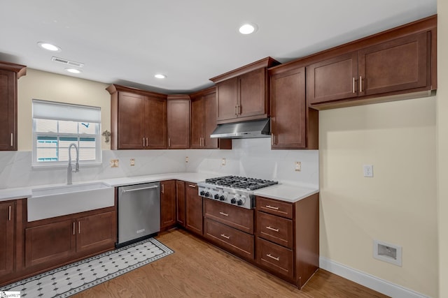 kitchen with backsplash, sink, light wood-type flooring, and appliances with stainless steel finishes