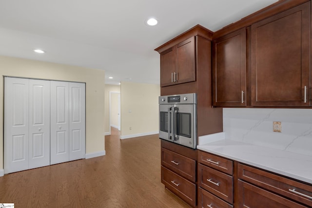 kitchen featuring dark brown cabinetry, stainless steel oven, light stone counters, light hardwood / wood-style flooring, and decorative backsplash