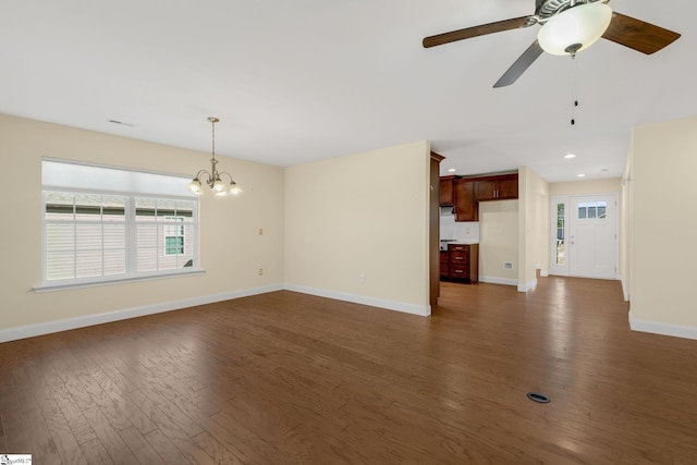 unfurnished living room with ceiling fan with notable chandelier and dark wood-type flooring