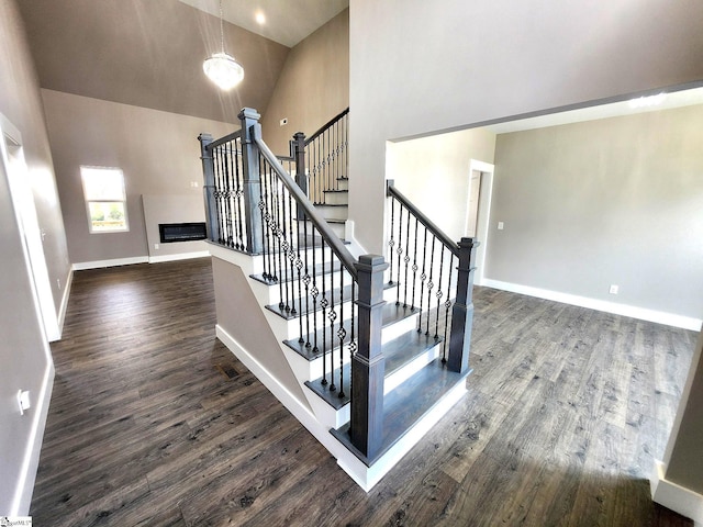 stairway with hardwood / wood-style floors, a notable chandelier, and high vaulted ceiling