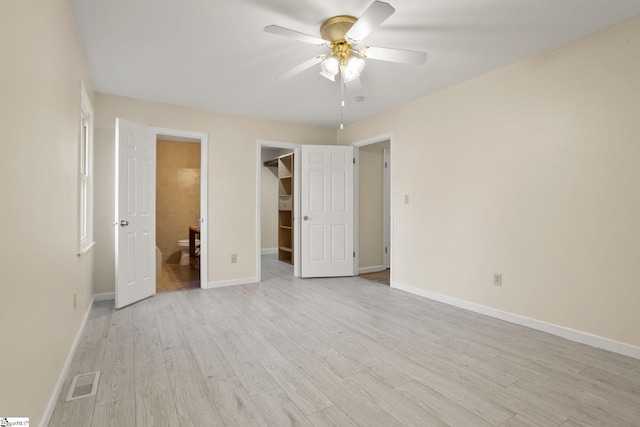 unfurnished bedroom with a closet, ensuite bath, light wood-type flooring, a spacious closet, and ceiling fan