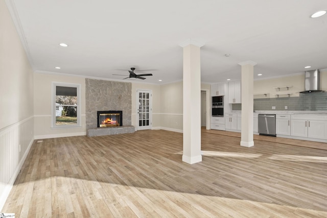 unfurnished living room featuring light hardwood / wood-style flooring, ceiling fan, a stone fireplace, and crown molding