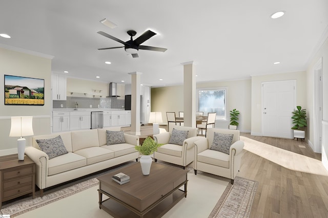 living room featuring sink, decorative columns, light hardwood / wood-style floors, ceiling fan, and ornamental molding