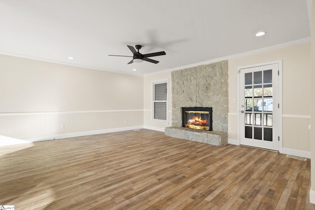 unfurnished living room with light wood-type flooring, crown molding, a stone fireplace, and ceiling fan