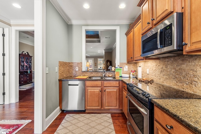 kitchen with sink, dark hardwood / wood-style floors, dark stone counters, appliances with stainless steel finishes, and ornamental molding