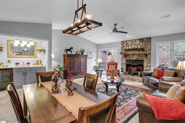 dining room featuring vaulted ceiling, light colored carpet, wine cooler, and a stone fireplace