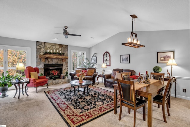 carpeted dining area with ceiling fan, a stone fireplace, and vaulted ceiling