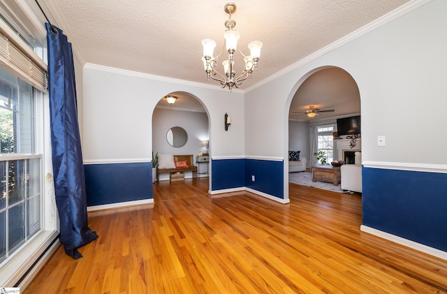 empty room with wood-type flooring, ceiling fan with notable chandelier, a textured ceiling, and crown molding