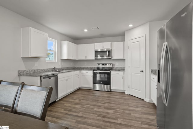 kitchen featuring white cabinets, appliances with stainless steel finishes, dark hardwood / wood-style floors, and light stone countertops