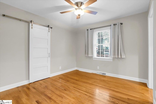 unfurnished bedroom featuring a barn door, ceiling fan, and hardwood / wood-style flooring